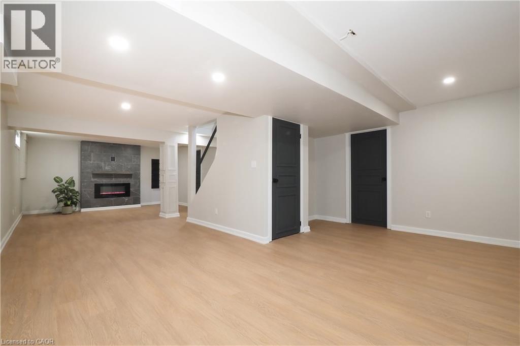 Spacious finished basement featuring wood-finish flooring, recessed lighting, and a modern electric fireplace with a dark stone-tile surround - 27 Scenic Wood Crescent, Kitchener, ON - Indoor With Fireplace