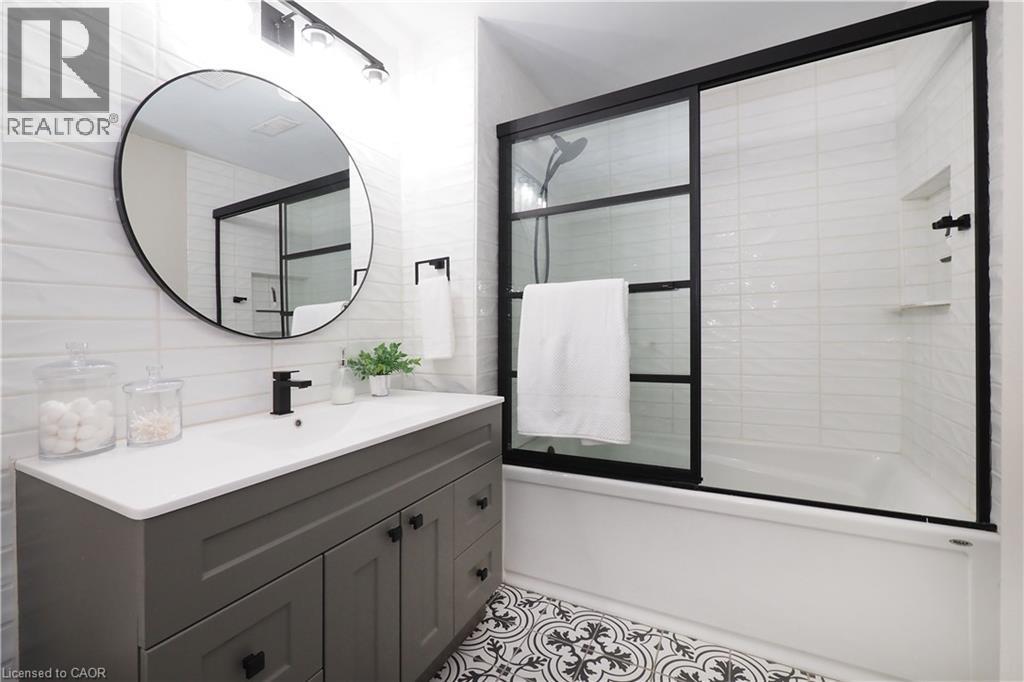 Bathroom featuring a gray vanity with an integrated sink, matte black fixtures, a round wall mirror, and a tub with sliding glass doors - 27 Scenic Wood Crescent, Kitchener, ON - Indoor Photo Showing Bathroom