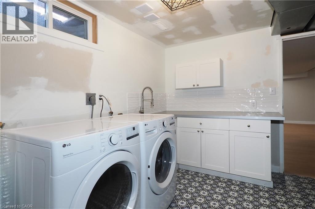 Laundry area with patterned tile flooring, shaker-style cabinetry, and a utility sink with a gooseneck faucet - 27 Scenic Wood Crescent, Kitchener, ON - Indoor Photo Showing Laundry Room