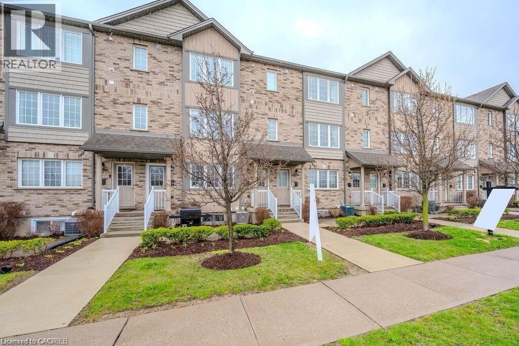 Brick and siding townhome exterior featuring multiple windows, individual covered entryways with white railings, a concrete walkway, and manicured landscaping with young trees - 275 Old Huron Road Unit# 21, Kitchener, ON - Outdoor With Facade