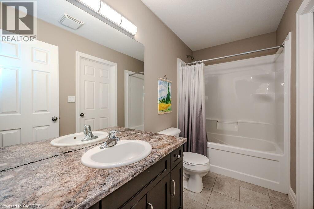 Bathroom featuring a double vanity with integrated sinks, a patterned countertop, dark wood-finish cabinetry, and a full-size bathtub with an overhead shower - 275 Old Huron Road Unit# 21, Kitchener, ON - Indoor Photo Showing Bathroom