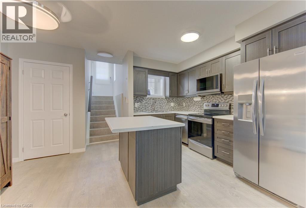 Kitchen with light wood-finish flooring, dark wood-finish cabinetry, stainless steel appliances, and a mosaic tile backsplash - 388 Old Huron Road Unit# 24A, Kitchener, ON - Indoor Photo Showing Kitchen With Upgraded Kitchen