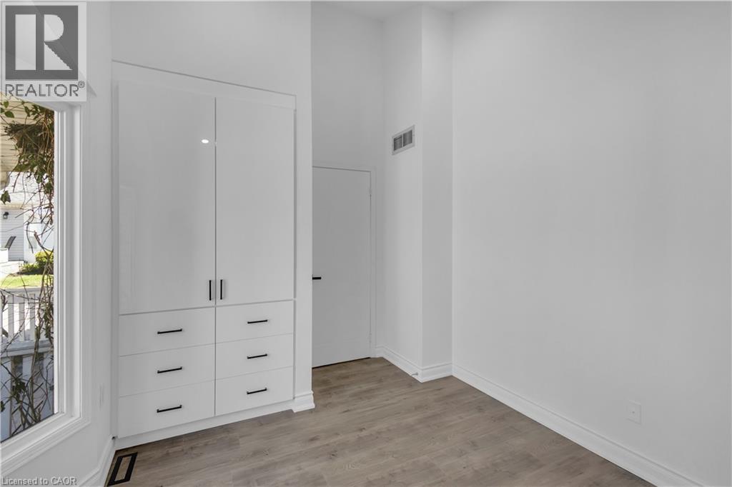 Integrated white cabinetry with black hardware, wood-finish flooring, and crisp white walls - 375 Silverbirch Boulevard, Hamilton, ON - Indoor Photo Showing Other Room