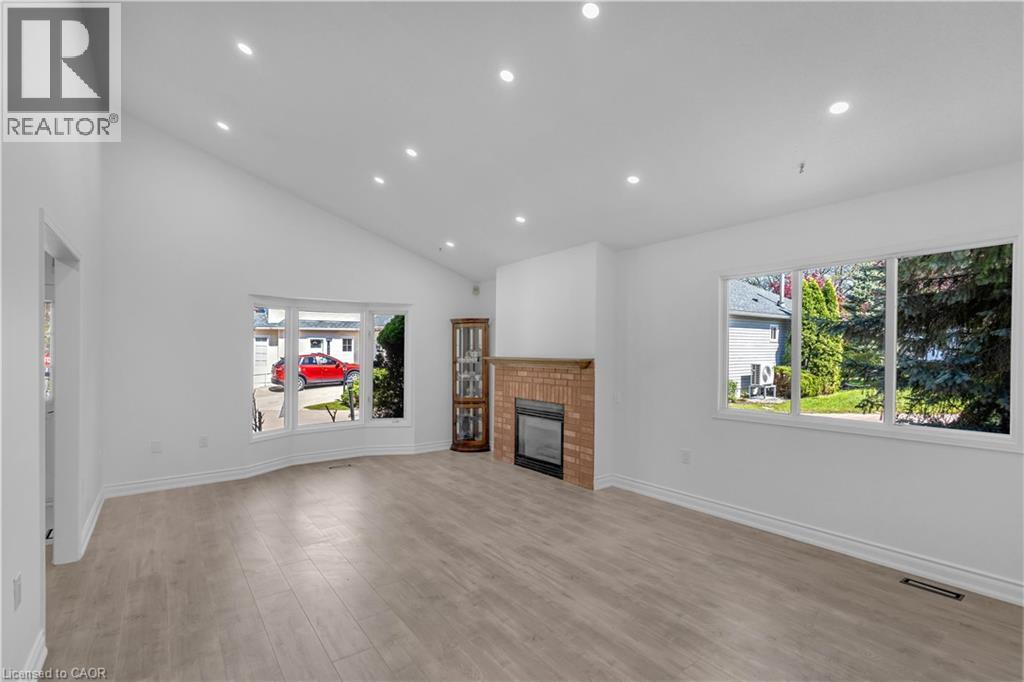 Spacious living area featuring wood-finish flooring, a brick-surround fireplace, and an angled ceiling with recessed lighting - 375 Silverbirch Boulevard, Hamilton, ON - Indoor Photo Showing Living Room With Fireplace