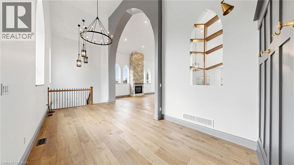Spacious entryway featuring wood-finish flooring, a tiered chandelier with lantern-style pendants, and an arched interior window with horizontal wood accents - 41 Talbot Road, Delhi, ON - Indoor Photo Showing Other Room