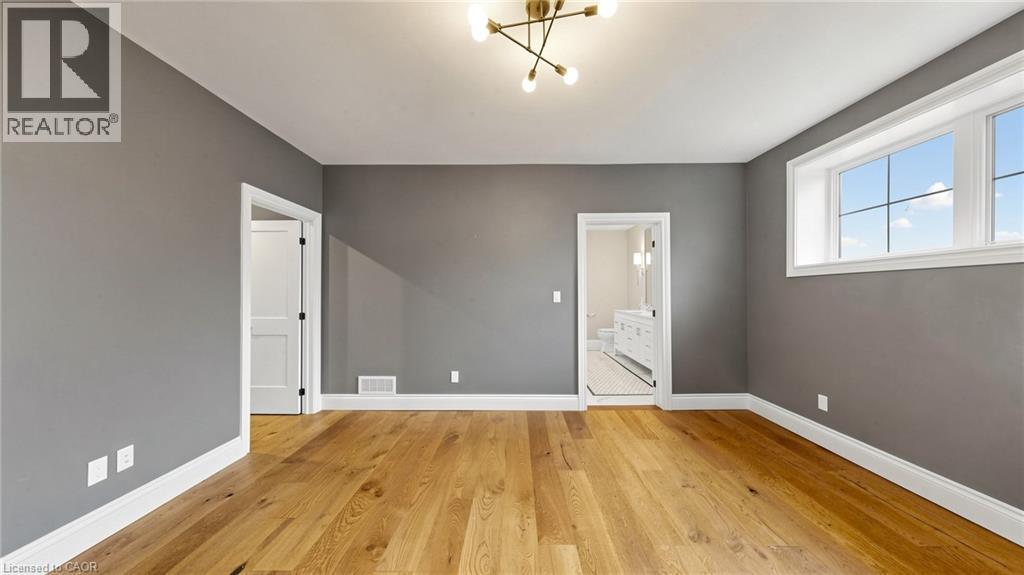 Spacious room featuring wood-finish flooring, neutral gray walls, white trim, a modern ceiling light fixture, and multiple windows - 41 Talbot Road, Delhi, ON - Indoor Photo Showing Other Room