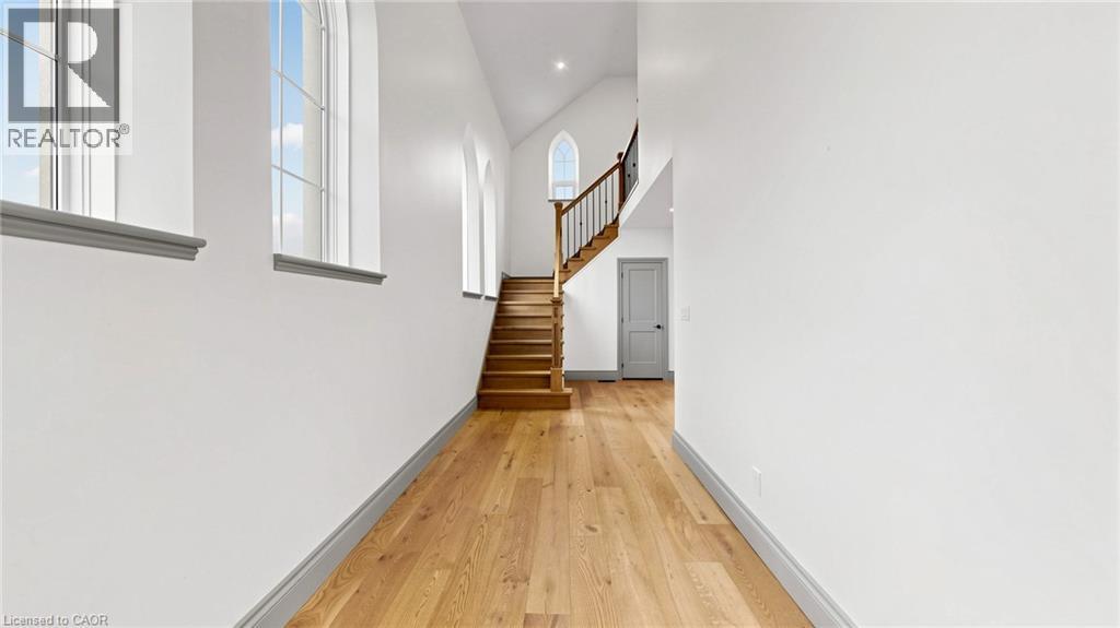 Vaulted ceilings with architectural windows, light wood-finish flooring, and a hardwood staircase with a wood and iron railing - 41 Talbot Road, Delhi, ON - Indoor Photo Showing Other Room