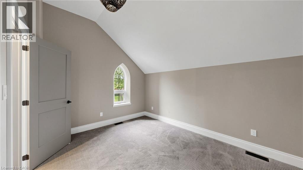 Vaulted ceiling room featuring a Gothic-style arched window, neutral wall paint, white trim, and gray carpet flooring - 41 Talbot Road, Delhi, ON - Indoor Photo Showing Other Room
