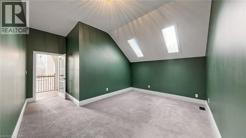 Attic room featuring two skylights, wall-to-wall carpeting, white baseboards, and a doorway with French doors opening to an interior balcony with a black metal railing - 41 Talbot Road, Delhi, ON - Indoor Photo Showing Other Room