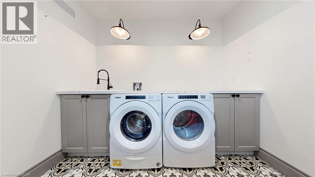 Laundry area featuring patterned floor tile, under-counter cabinetry, a mounted utility sink with a matte black faucet, and two industrial-style wall sconces - 41 Talbot Road, Delhi, ON - Indoor Photo Showing Laundry Room