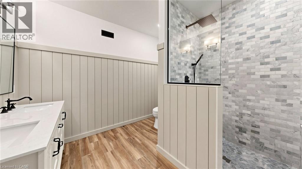 Bathroom featuring wood-finish flooring, board and batten wall paneling, a double vanity with matte black fixtures, a walk-in shower with glass enclosure, and subway tile walls - 41 Talbot Road, Delhi, ON -