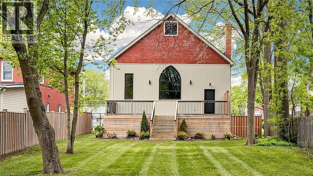 Rear exterior featuring a red brick gable, arched window, and horizontal cream siding - 41 Talbot Road, Delhi, ON - Outdoor