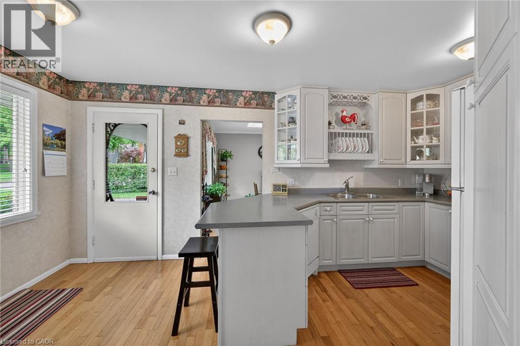 Kitchen featuring wood-finish flooring, white cabinetry, and a peninsula with countertop seating - 2 Summit Circle, Simcoe, ON - Indoor Photo Showing Kitchen With Double Sink