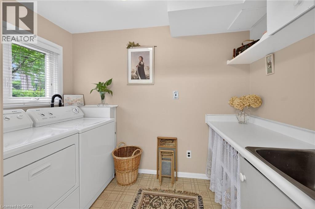 Laundry room featuring a window with horizontal blinds, built-in countertop with an integrated sink, wall-mounted shelving, and patterned vinyl flooring - 2 Summit Circle, Simcoe, ON - Indoor Photo Showing Laundry Room