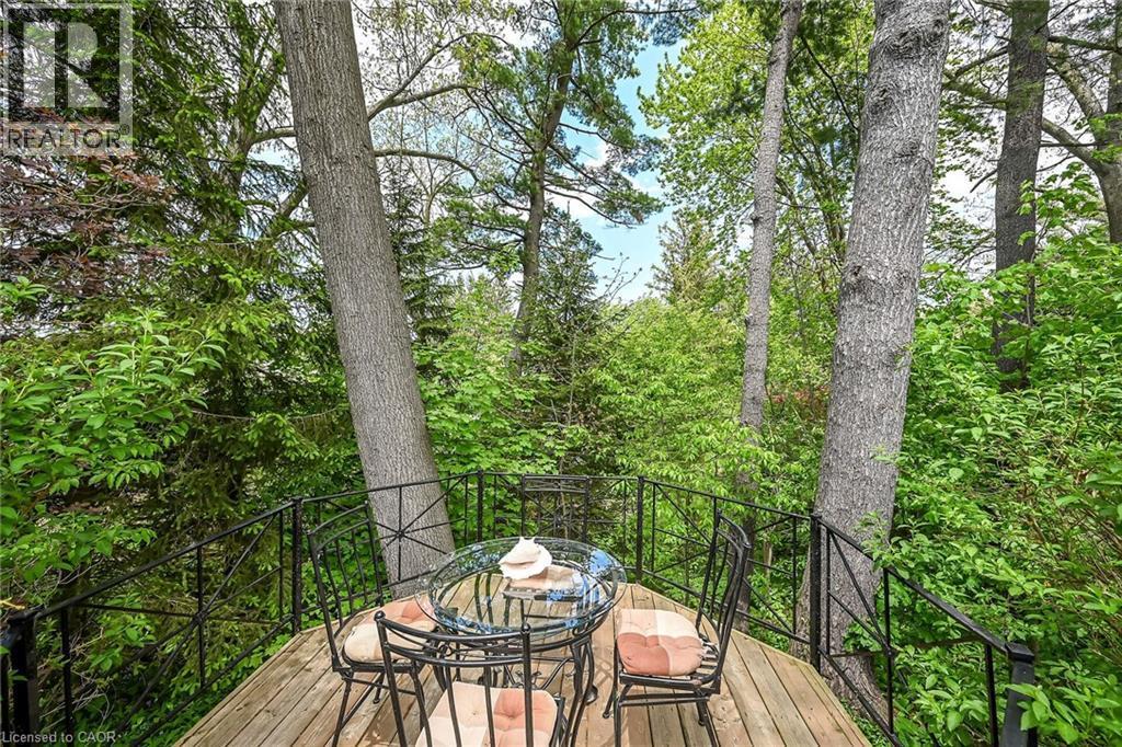 Elevated wood-deck balcony with black wrought-iron railing, surrounded by mature trees and lush foliage - 2 Summit Circle, Simcoe, ON - Outdoor With Deck Patio Veranda