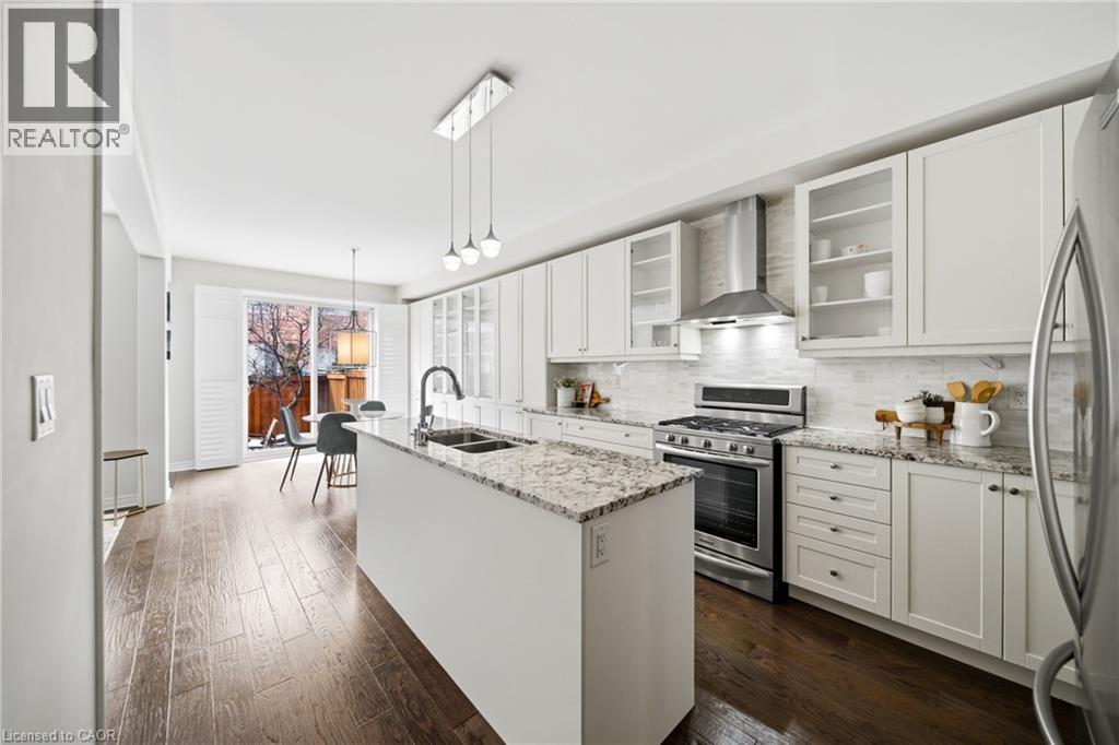 Kitchen featuring a center island with a granite countertop, white cabinetry with glass-front accents, stainless steel appliances, and wood-finish flooring - 2466 Village Common, Oakville, ON - Indoor Photo Showing Kitchen With Double Sink With Upgraded Kitchen