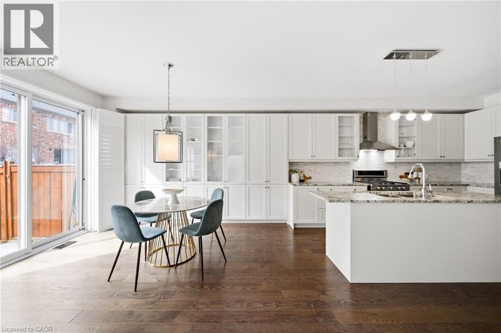 Open-concept kitchen and dining area featuring rich wood-finish flooring, white cabinetry with glass-front accents, and a central island with a light-toned countertop - 2466 Village Common, Oakville, ON - Indoor