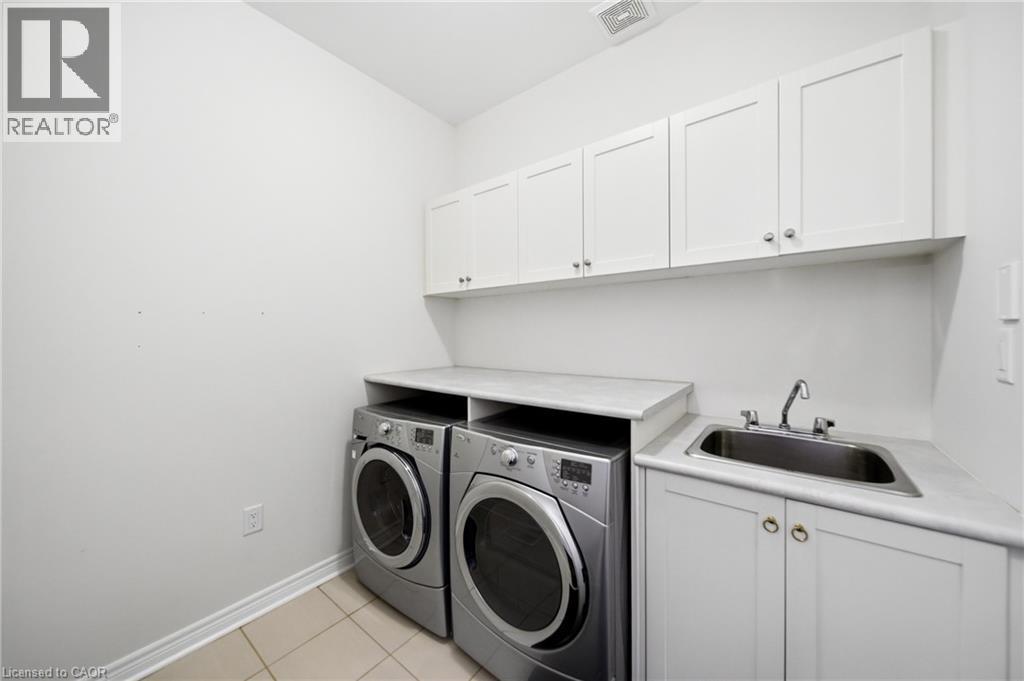 Dedicated laundry room featuring white shaker-style cabinetry, a utility sink with chrome fixtures, and a light-colored countertop - 2466 Village Common, Oakville, ON - Indoor Photo Showing Laundry Room
