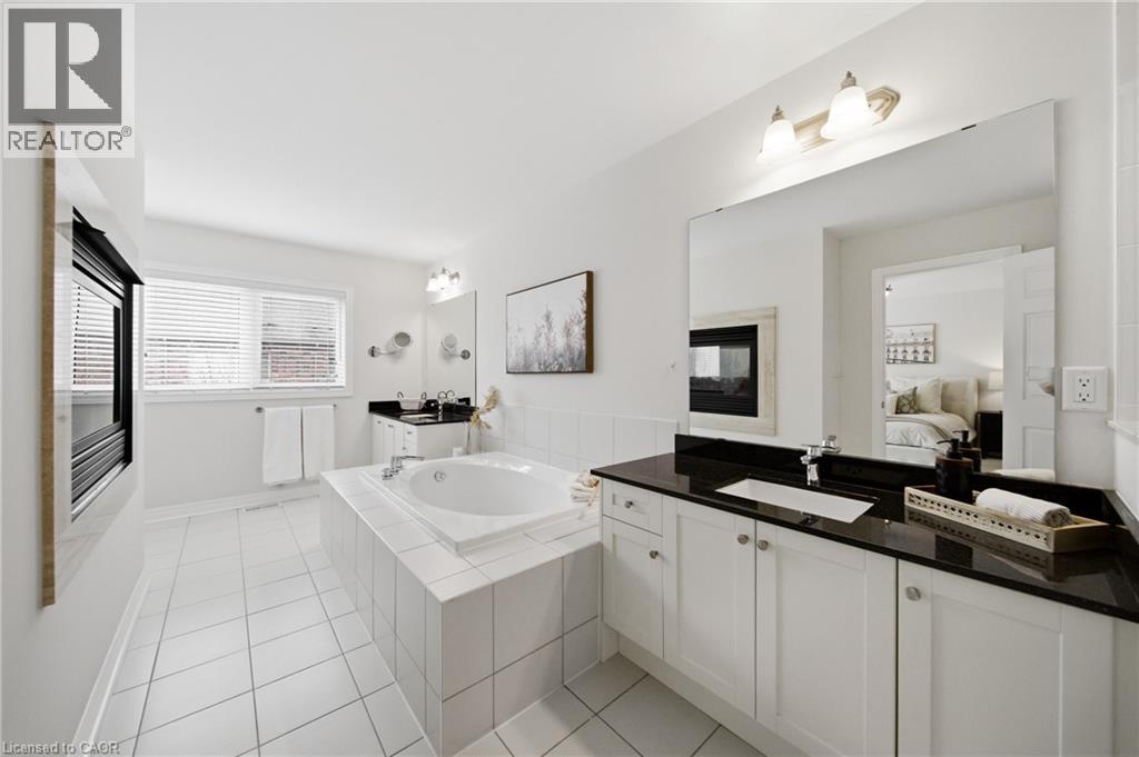Spacious bathroom featuring a built-in soaking tub, dual vanity with black countertops, integrated fireplace, expansive wall mirror, and white tile flooring - 2466 Village Common, Oakville, ON - Indoor Photo Showing Bathroom