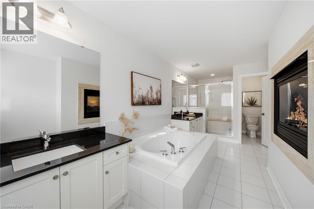 Bathroom featuring an integrated gas fireplace, a built-in soaking tub, dual vanity with dark countertops, and a glass-enclosed shower with a built-in bench - 2466 Village Common, Oakville, ON - Indoor Photo Showing Bathroom