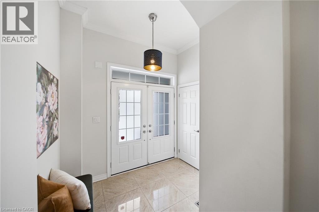 Foyer featuring white double entry doors with decorative glass panels and transom window, light-toned tile flooring, a contemporary pendant light fixture, and crown molding accents - 2466 Village Common, Oakville, ON - Indoor Photo Showing Other Room