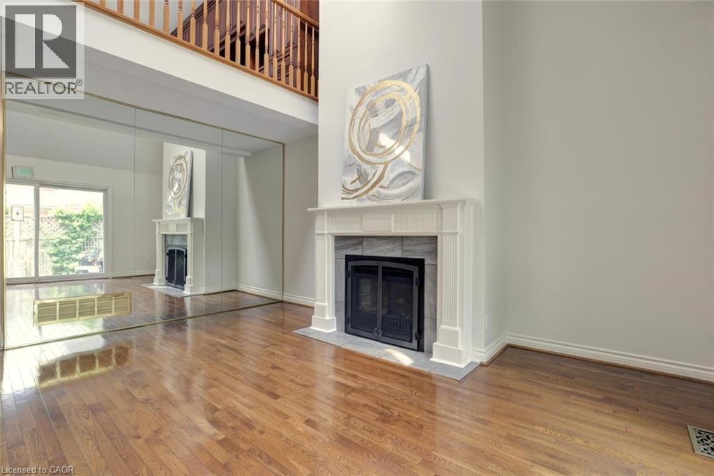 Living area featuring wood-finish flooring and a fireplace with a white mantel and stone surround - 463 Blathwayte Lane, Burlington, ON - Indoor Photo Showing Living Room With Fireplace