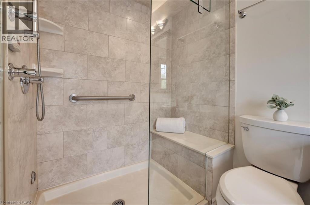 Walk-in shower featuring light-toned rectangular wall tiles, a built-in bench, a chrome-finish handheld shower fixture, a grab bar, and a clear glass enclosure - 463 Blathwayte Lane, Burlington, ON - Indoor Photo Showing Bathroom