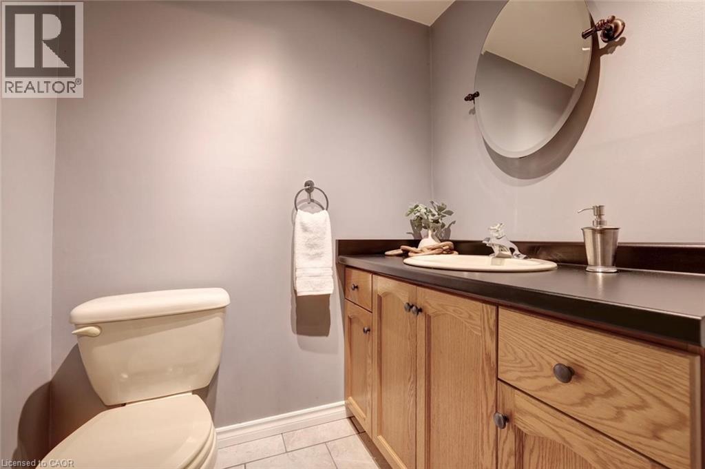 Vanity featuring wood-finish cabinetry with dark hardware, a dark countertop, and an oval mirror - 463 Blathwayte Lane, Burlington, ON - Indoor Photo Showing Bathroom
