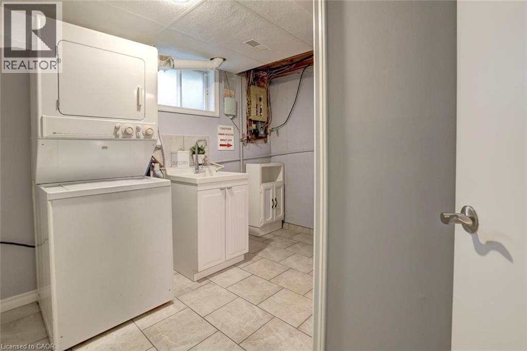 Dedicated laundry area featuring a stacked washer and dryer unit, tiled flooring, a utility sink with white cabinetry, and a frosted window - 463 Blathwayte Lane, Burlington, ON - Indoor Photo Showing Laundry Room