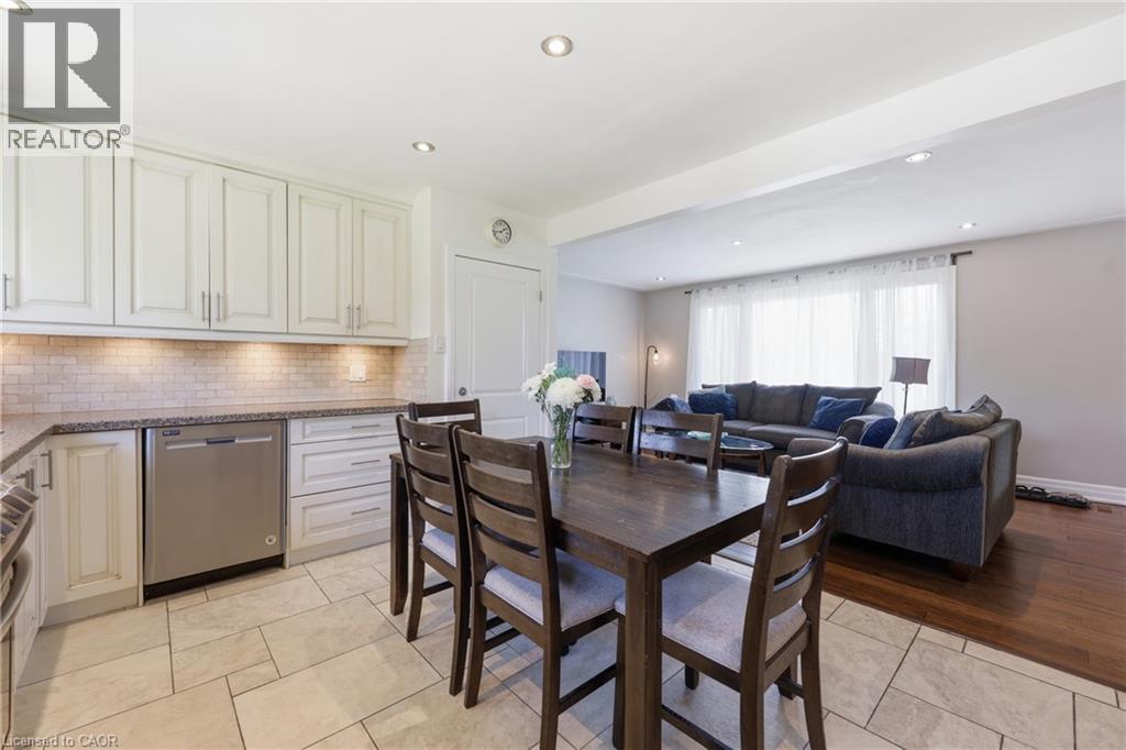Open-concept kitchen and living area featuring white cabinetry, a tiled backsplash, stainless steel appliances, and a dining space with wood-finish flooring in the adjacent living room - 168 Nugent Drive, Hamilton, ON - Indoor