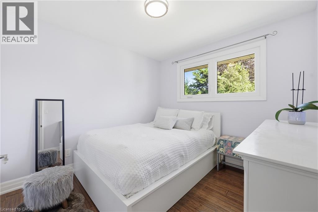 Bright room featuring wood-finish flooring, a white trim window, and a ceiling-mounted light fixture - 168 Nugent Drive, Hamilton, ON - Indoor Photo Showing Bedroom