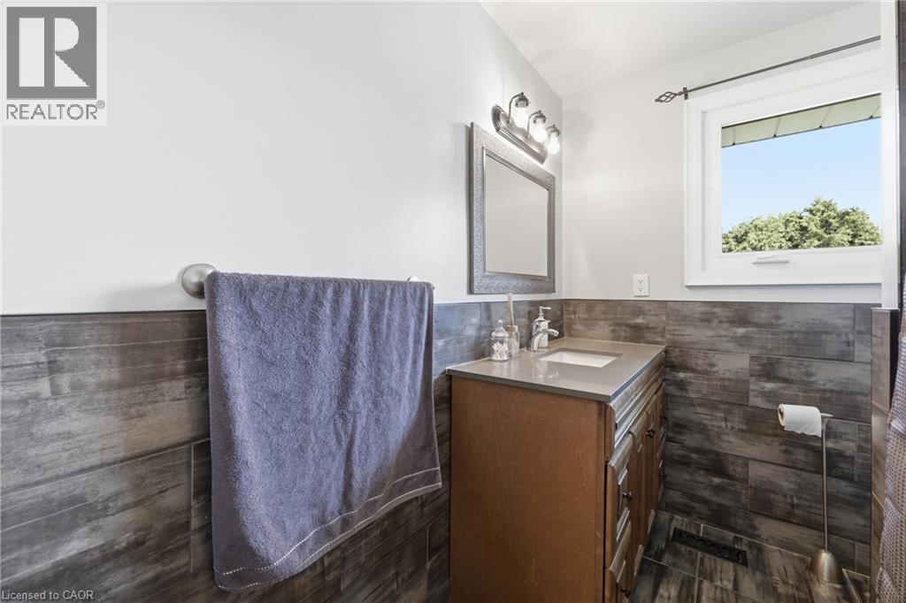 Bathroom featuring wood-finish wall paneling, a single vanity with a light-toned countertop, and a window with exterior tree scenery - 168 Nugent Drive, Hamilton, ON - Indoor Photo Showing Bathroom