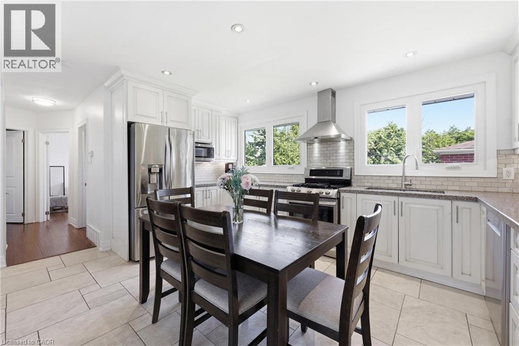 Bright kitchen featuring white cabinetry, stainless steel appliances, light-toned tile flooring, and multiple windows - 168 Nugent Drive, Hamilton, ON - Indoor