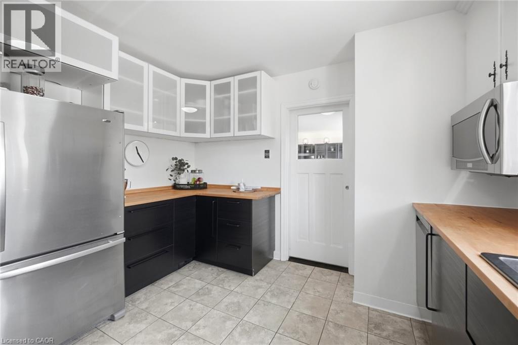 Kitchen featuring stainless steel appliances, black base cabinetry, wood-finish countertops, white upper cabinets with frosted glass panels, and tile flooring - 94 Clarendon Avenue, Hamilton, ON - Indoor Photo Showing Kitchen