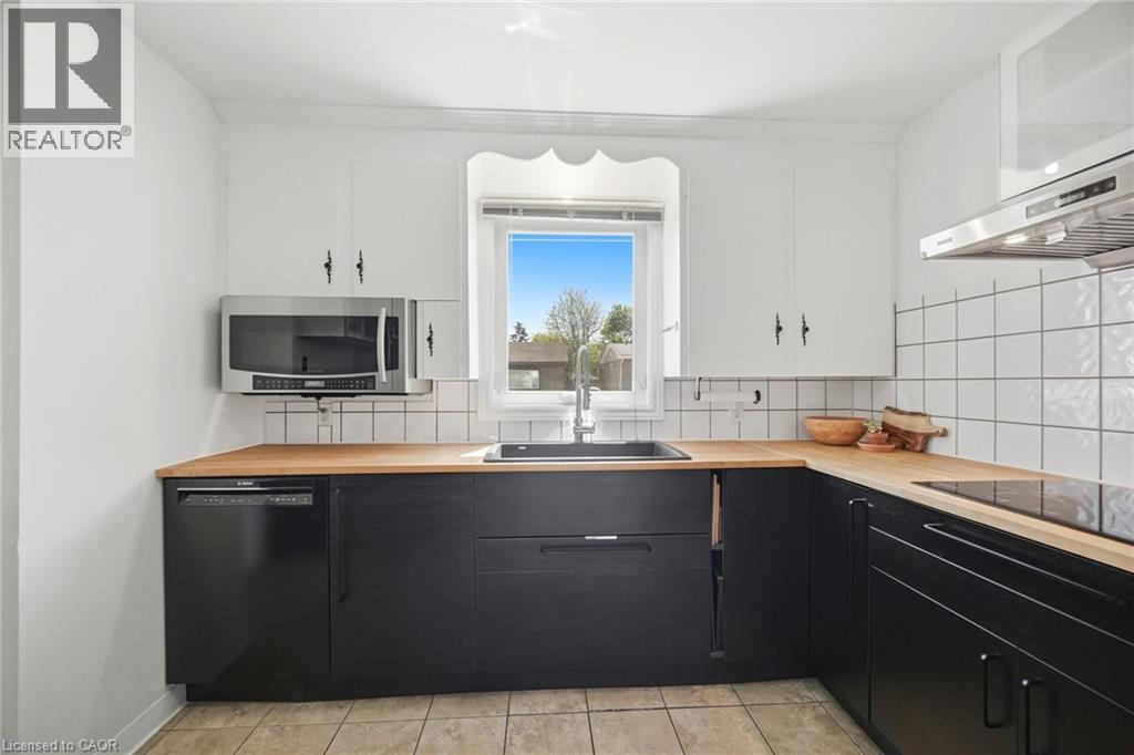 Kitchen featuring black base cabinetry, white upper cabinetry, natural wood-finish countertops, and a white square tile backsplash - 94 Clarendon Avenue, Hamilton, ON - Indoor Photo Showing Kitchen