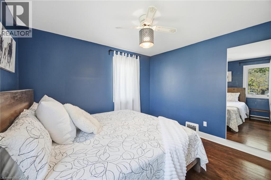 Bedroom featuring hardwood flooring, a ceiling fan with integrated lighting, a window with sheer white curtains, and a full-length wall mirror - 94 Clarendon Avenue, Hamilton, ON - Indoor Photo Showing Bedroom