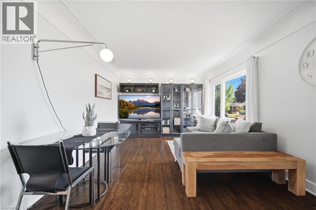 Open-concept living area featuring wood-finish flooring, a contemporary glass-top table, a wall-mounted articulating light fixture, built-in shelving, and a large bay window - 94 Clarendon Avenue, Hamilton, ON - Indoor