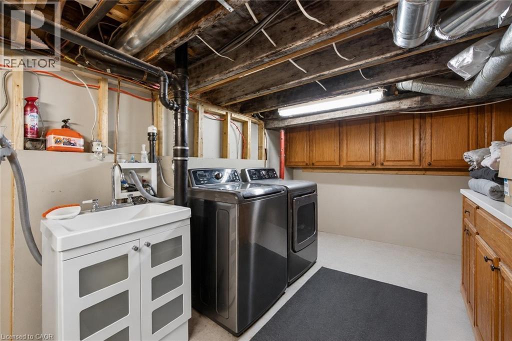 Utility room featuring a laundry sink with white vanity, dark-finish laundry appliances, and ample wall-mounted wood cabinetry - 147 Strachan Street E, Hamilton, ON - Indoor Photo Showing Laundry Room