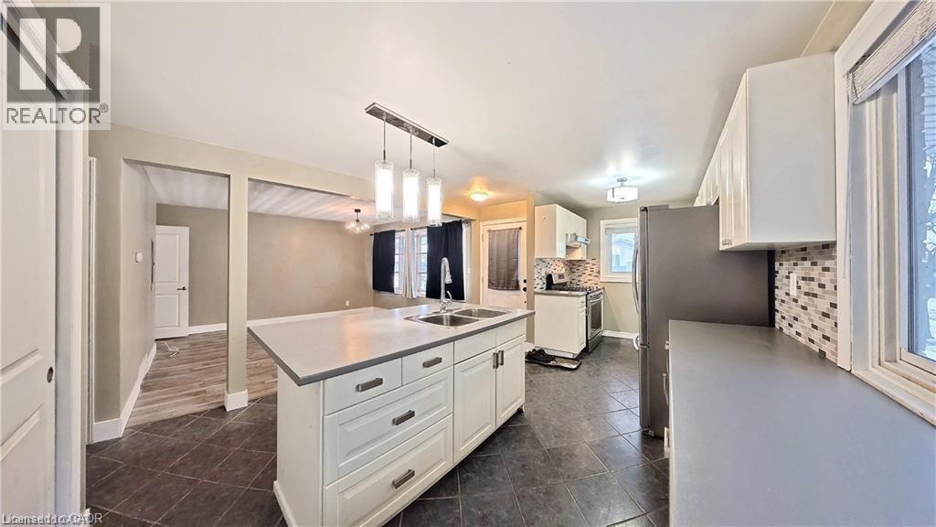 Kitchen featuring a central island with dual sinks, white shaker-style cabinetry, dark tile flooring, and a mosaic tile backsplash - 61 Bosworth Crescent Unit# Upper, Kitchener, ON - Indoor Photo Showing Kitchen With Double Sink