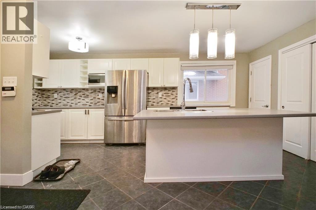 Contemporary kitchen featuring a substantial island with integrated sink, stainless steel appliances, mosaic tile backsplash, white cabinetry, and dark tile flooring - 61 Bosworth Crescent Unit# Upper, Kitchener, ON - Indoor Photo Showing Kitchen With Stainless Steel Kitchen