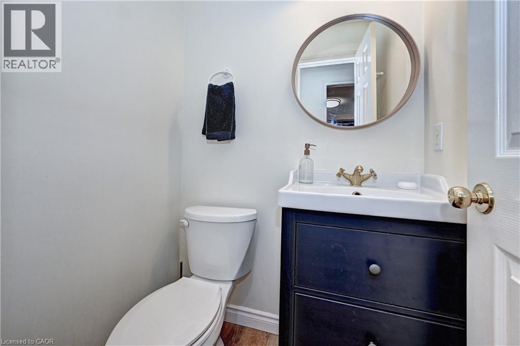Compact powder room featuring a white toilet, dark wood-finish vanity with drawer storage, and a circular wall mirror - 519 Yorkshire Drive, Waterloo, ON - Indoor Photo Showing Bathroom