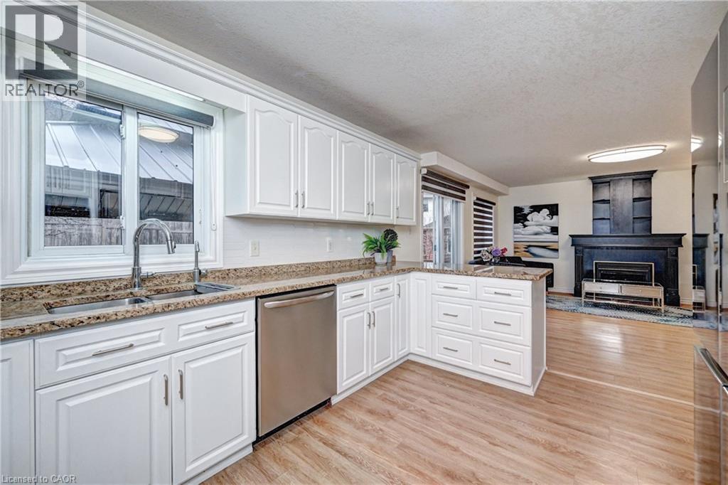 Bright kitchen featuring white cabinetry, granite countertops, stainless steel dishwasher, and wood-finish flooring - 519 Yorkshire Drive, Waterloo, ON - Indoor Photo Showing Kitchen With Double Sink