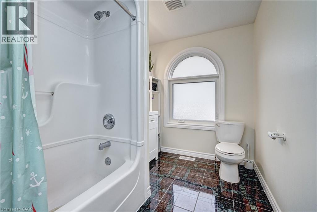 Bathroom featuring a tub/shower combination with chrome fixtures, a toilet, an arched window, and dark patterned tile flooring - 519 Yorkshire Drive, Waterloo, ON - Indoor Photo Showing Bathroom