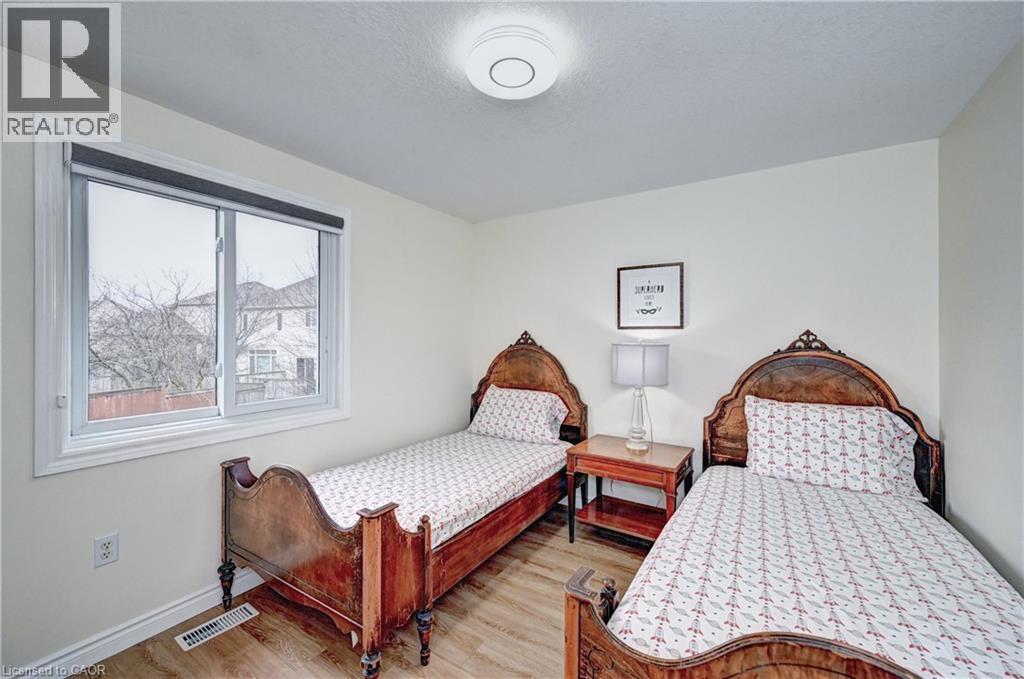 Neutral wall paint and wood-finish flooring characterize this room, featuring a white trim window with roller shade and a ceiling-mounted light fixture - 519 Yorkshire Drive, Waterloo, ON - Indoor Photo Showing Bedroom