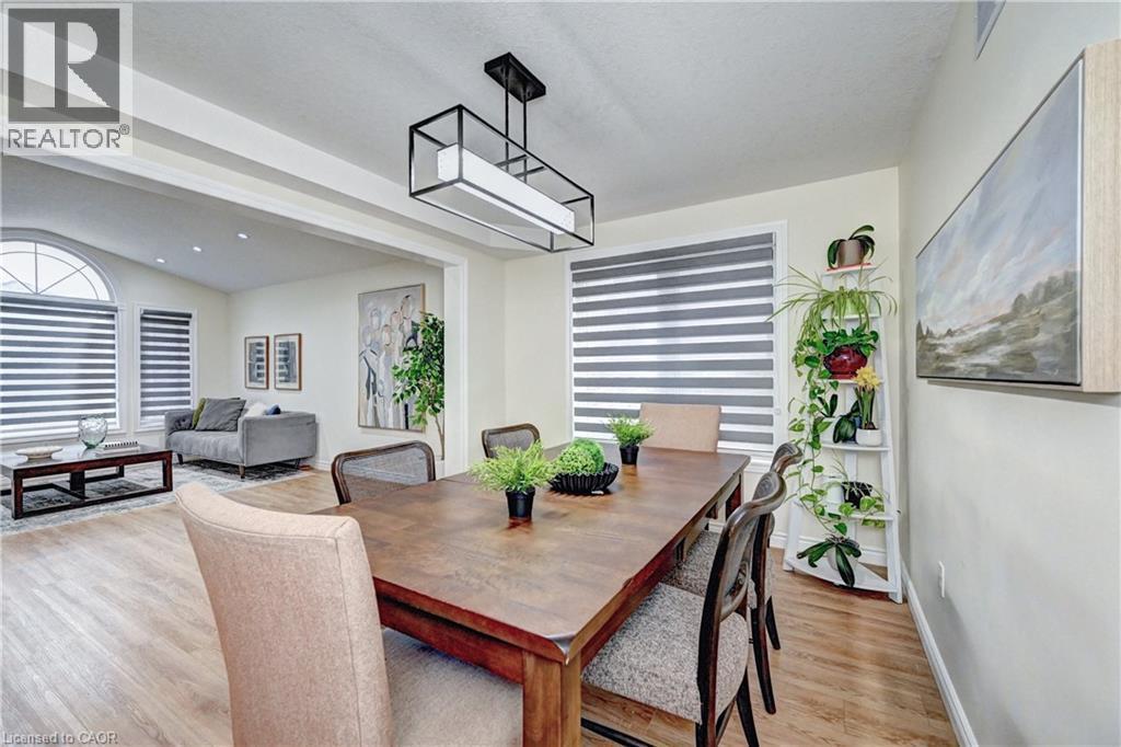 Dining area featuring wood-finish flooring, a contemporary linear chandelier, and a large window with horizontal blinds - 519 Yorkshire Drive, Waterloo, ON - Indoor Photo Showing Dining Room