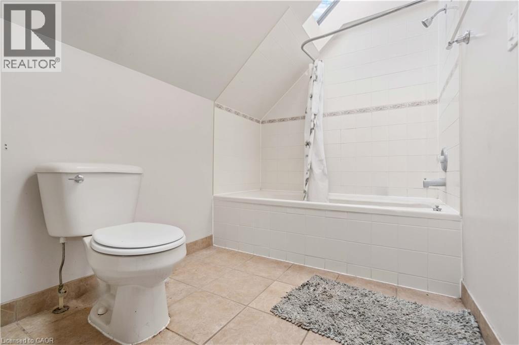 Bathroom featuring a white toilet, tiled flooring, a bathtub with shower, white subway tile surround, and a skylight - 151 Louisa Street, Kitchener, ON - Indoor Photo Showing Bathroom