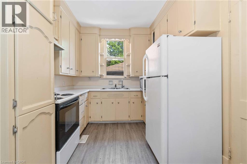 Galley kitchen featuring light-toned cabinetry, white countertops, and wood-finish flooring - 151 Louisa Street, Kitchener, ON - Indoor Photo Showing Kitchen With Double Sink