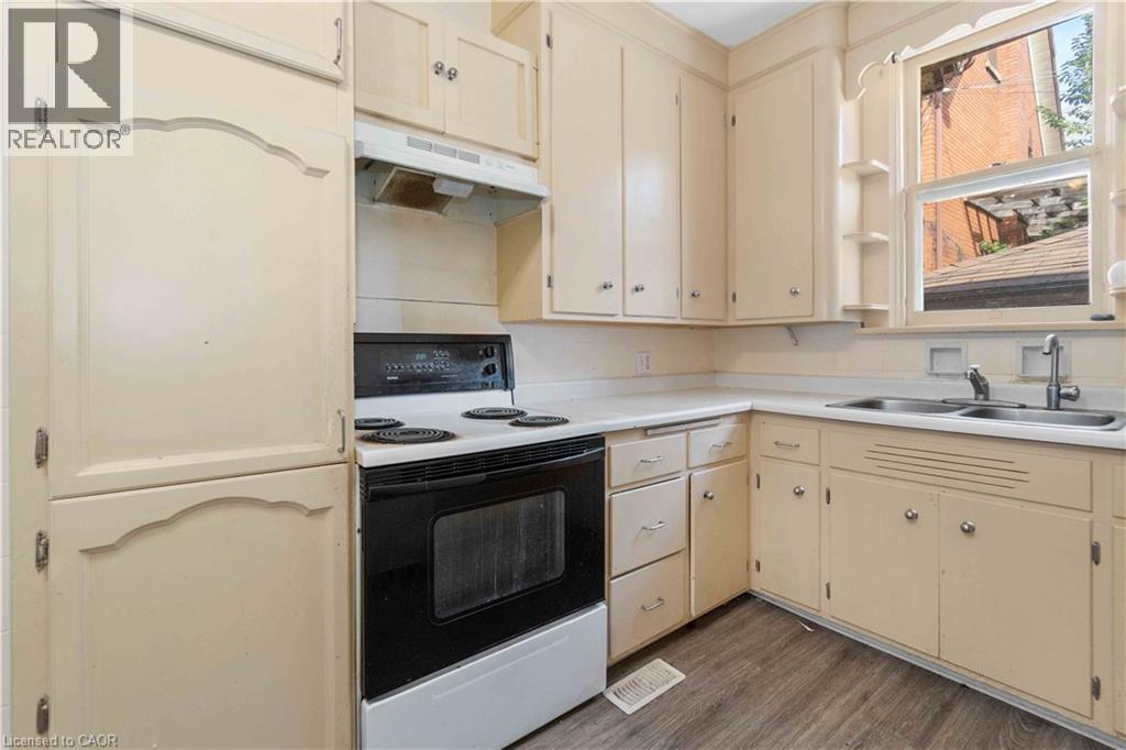 Cream-colored cabinetry with decorative accents, a black electric range with an overhead exhaust, a double basin stainless steel sink, light-toned countertops, and wood-finish flooring - 151 Louisa Street, Kitchener, ON - Indoor Photo Showing Kitchen With Double Sink