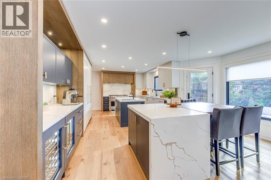 Open-concept kitchen featuring wood-finish flooring, recessed lighting, and a large central island with a waterfall countertop - 54 Deerview Avenue, Ancaster, ON - Indoor Photo Showing Kitchen With Upgraded Kitchen