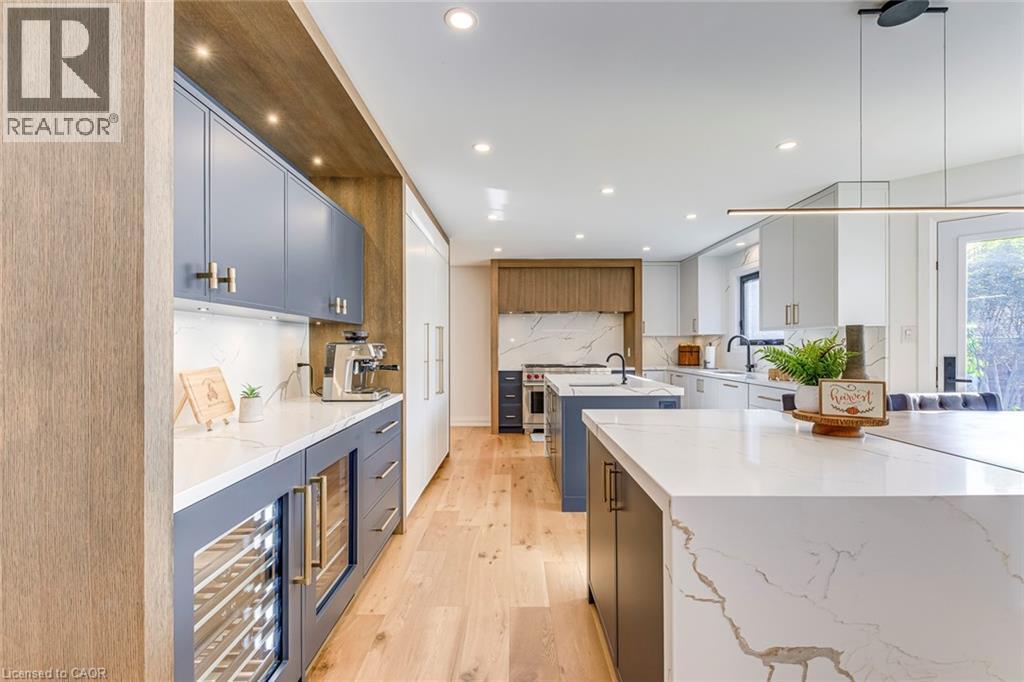 Contemporary kitchen featuring light wood-finish flooring, recessed lighting, and a large central island with a waterfall countertop - 54 Deerview Avenue, Ancaster, ON - Indoor Photo Showing Kitchen With Upgraded Kitchen